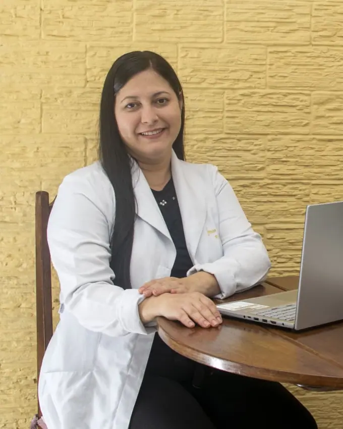 Jeanice Neves Ferreira Carneiro, fisioterapeuta do trabalho e ergonomista, sentada à mesa de trabalho com notebook